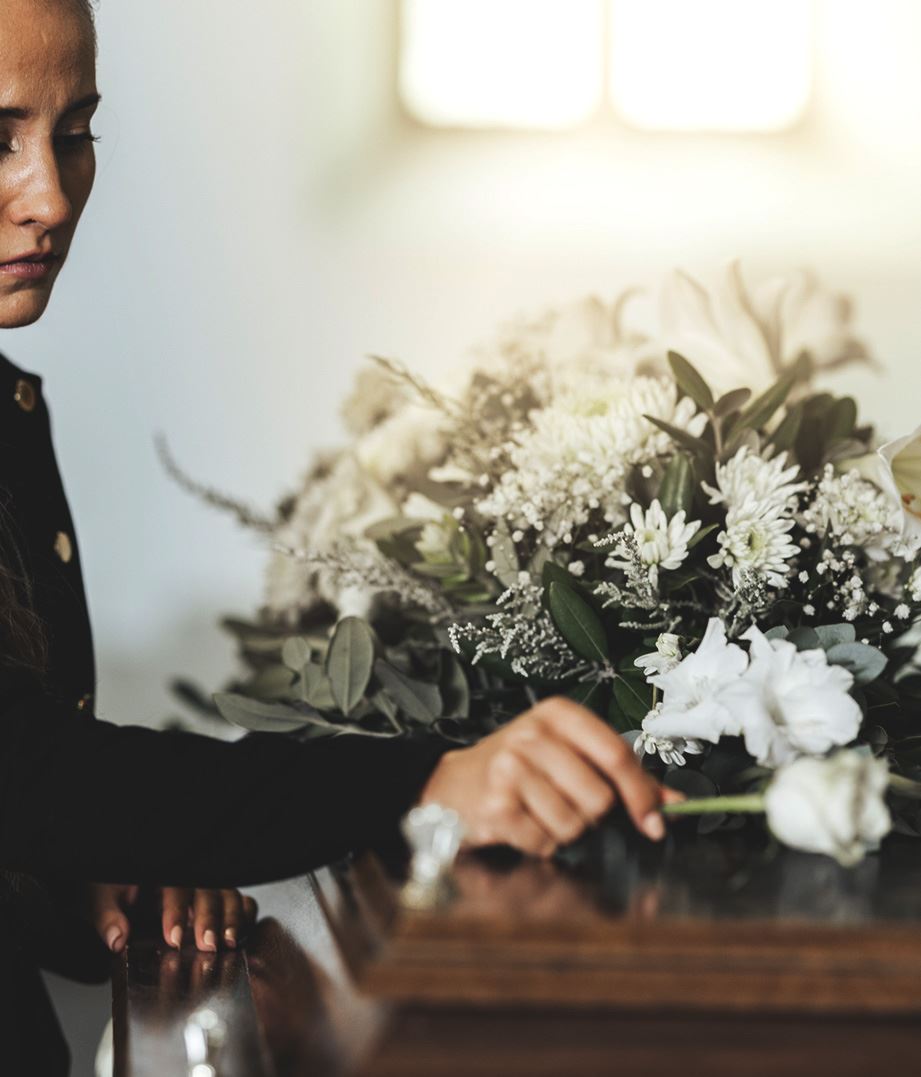 Person at a funeral somberly placing a white rose on top of a casket