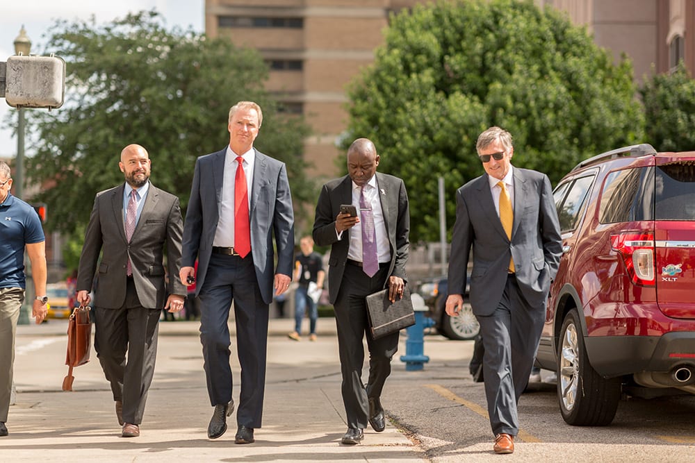 Attorney team, walking. Four men wearing suits. Included are Bob Hilliard and Ben Crump.