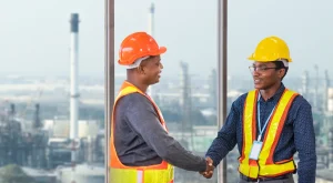 Two oil and gas workers in protective gear and shaking hands.